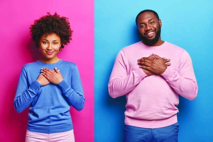 Touched dark skinned sister and brother appreciate parents care, constant support, keep palms on heart, express gratitude and warm feelings, smile pleasantly, isolated over pink and blue background
