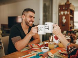 Two people happily clinking mugs across a kitchen table